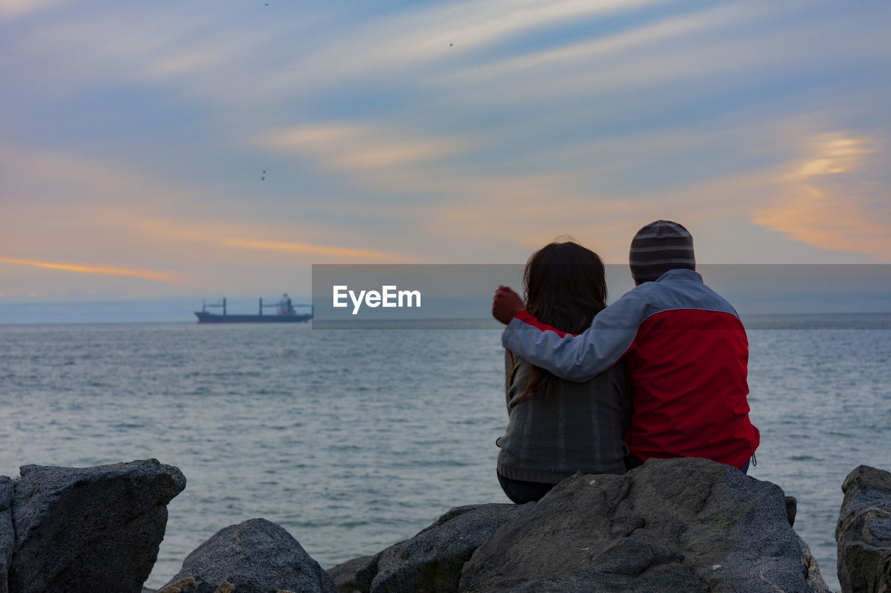 REAR VIEW OF COUPLE LOOKING AT SEA AGAINST SKY