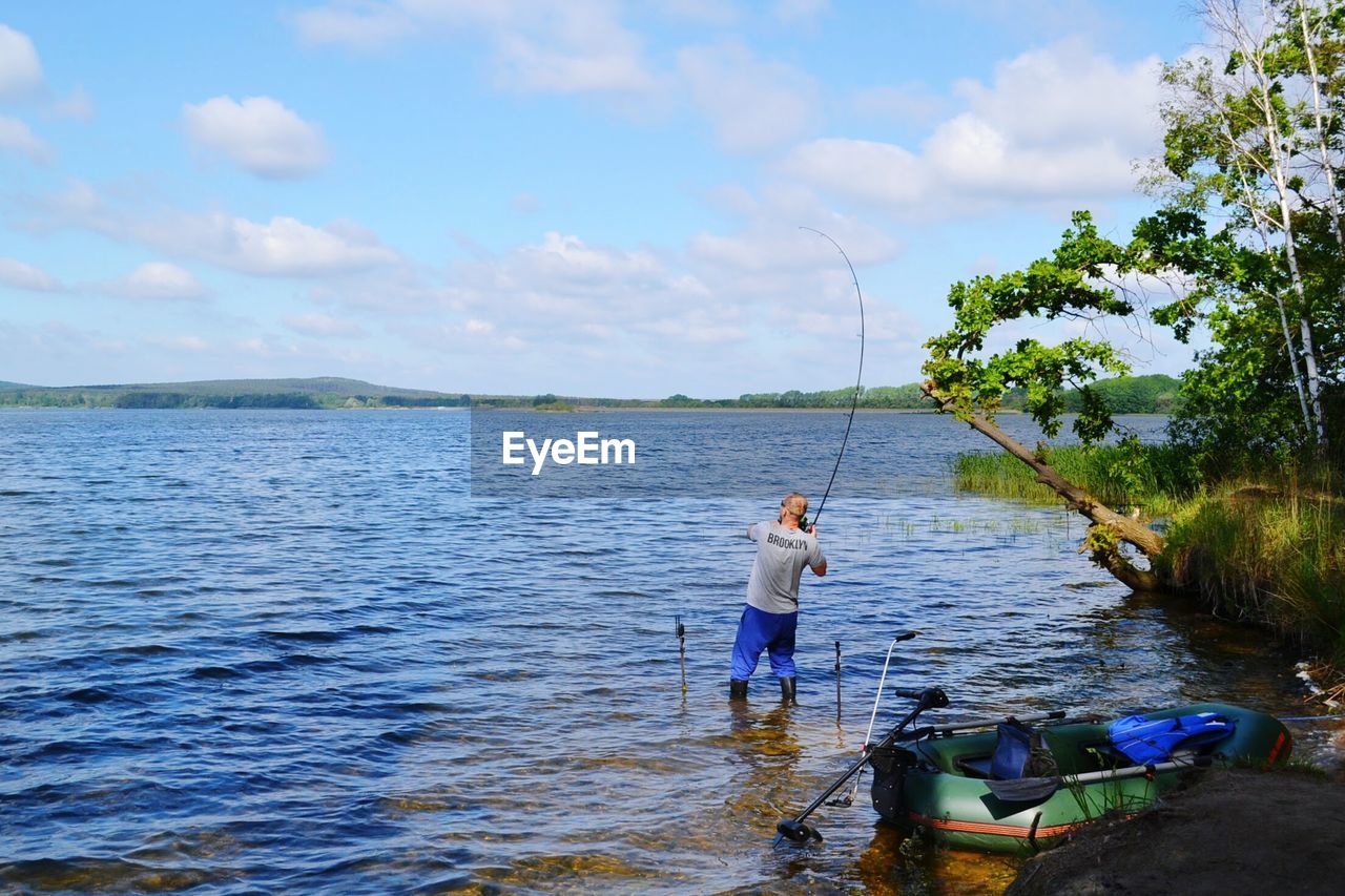 REAR VIEW OF MAN FISHING AT RIVER