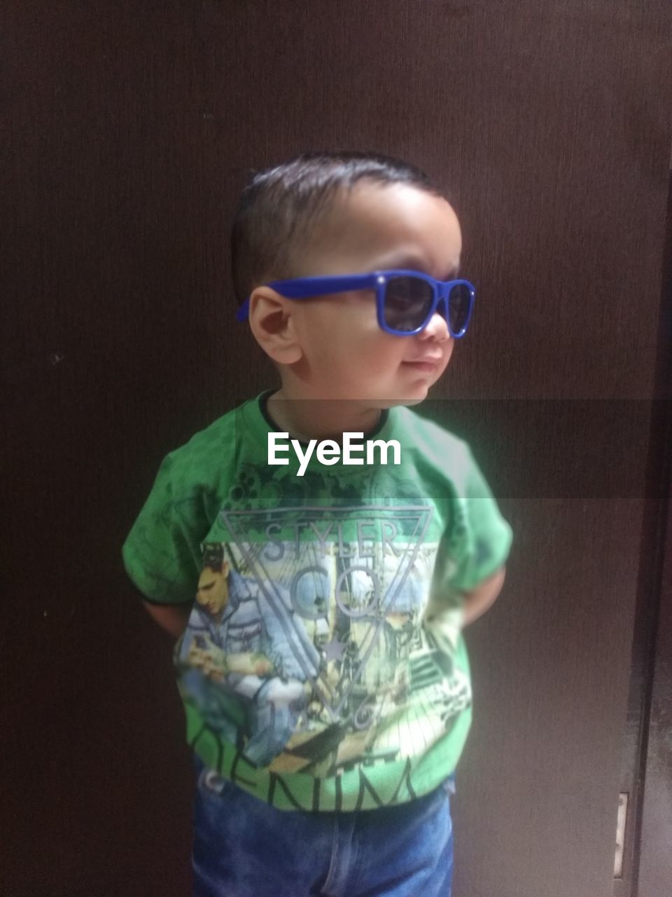 BOY WEARING SUNGLASSES STANDING AGAINST CURTAIN