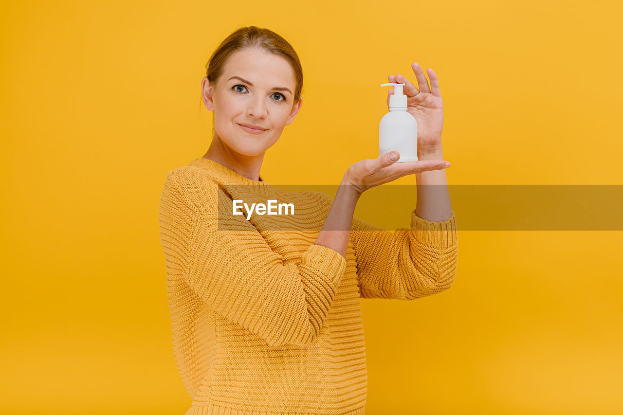 Portrait of smiling young woman against yellow background