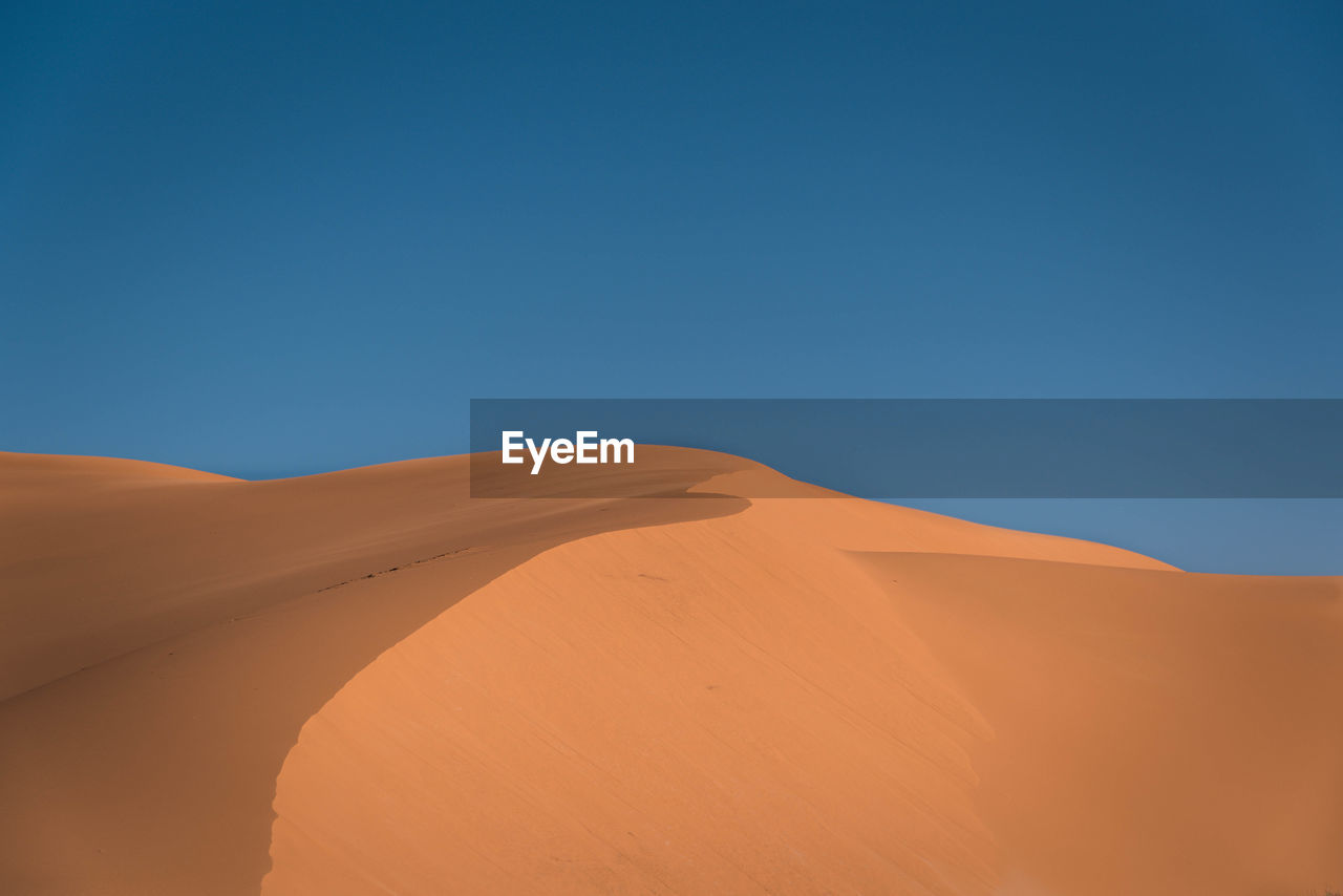Low angle view of sand dune against clear blue sky