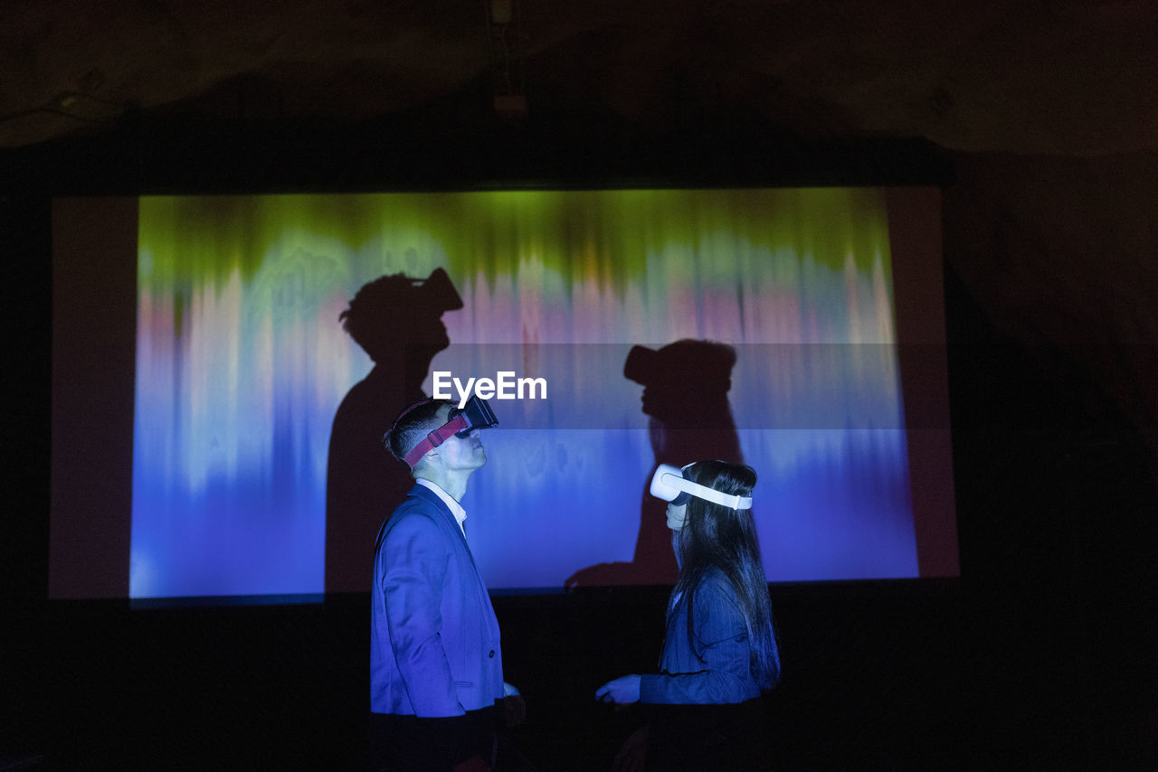 Multiracial business colleagues watching through vr glasses in illuminated exhibition center