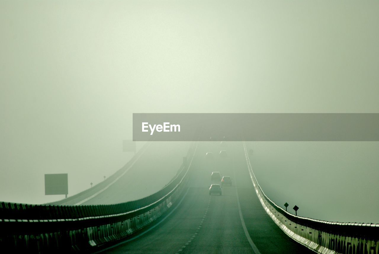 transportation, fog, road, the way forward, nature, architecture, mode of transportation, morning, city, copy space, built structure, no people, sky, highway, street, travel, outdoors, bridge, darkness, mist, environment, motor vehicle, car, motion, sign, light, curve, travel destinations