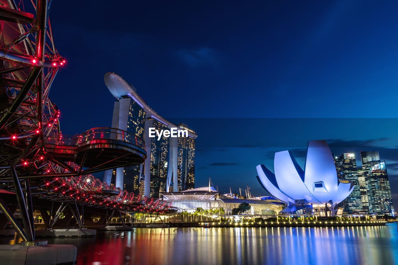 Low angle view of illuminated buildings by river against sky in city at night