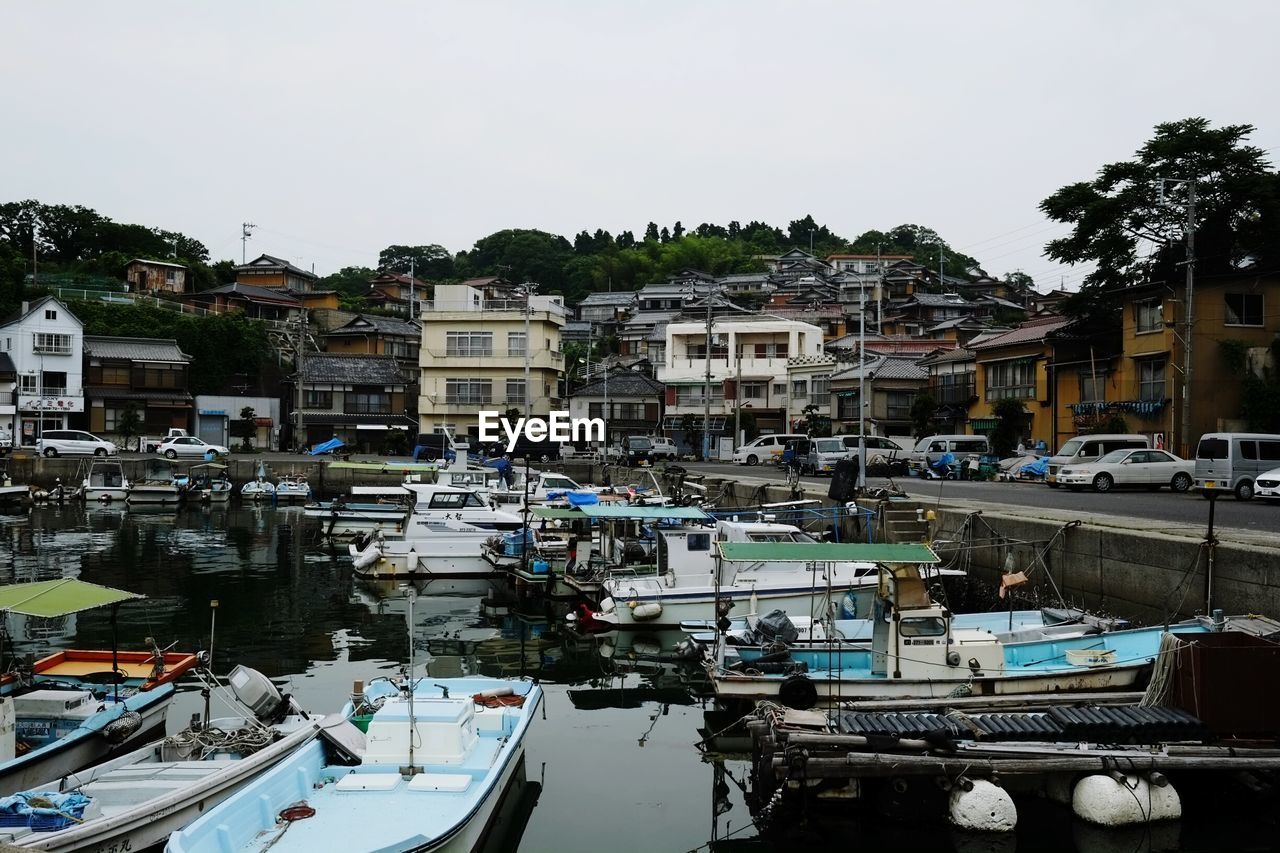 Boats moored in harbor on lake by street and buildings