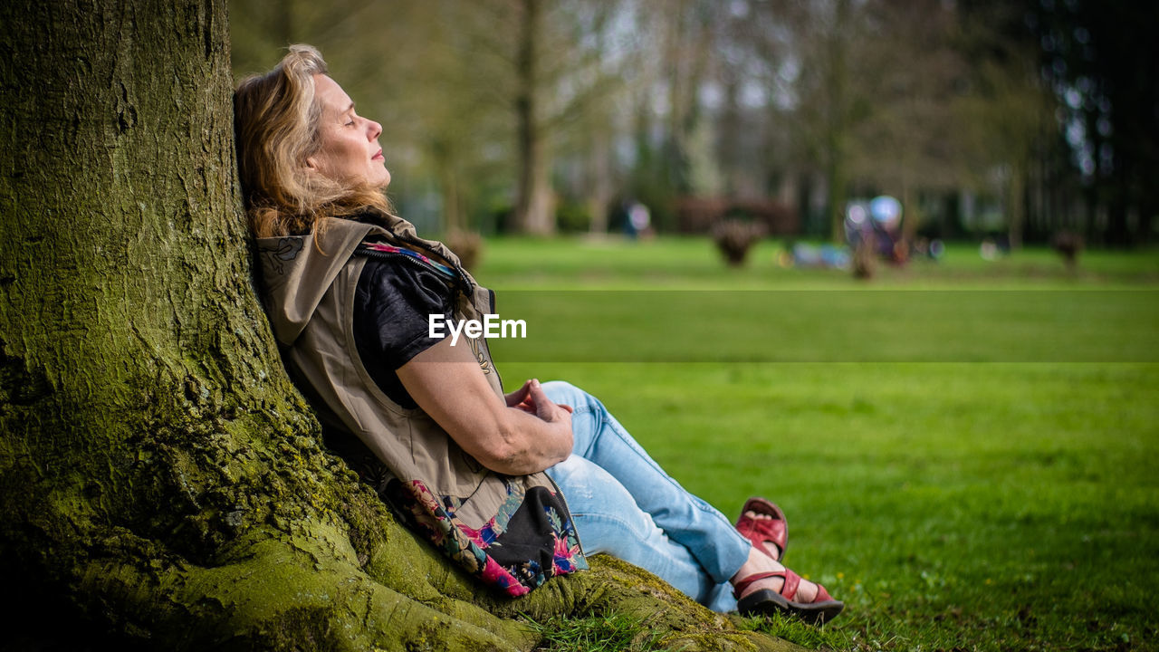 Woman sitting by tree trunk at park