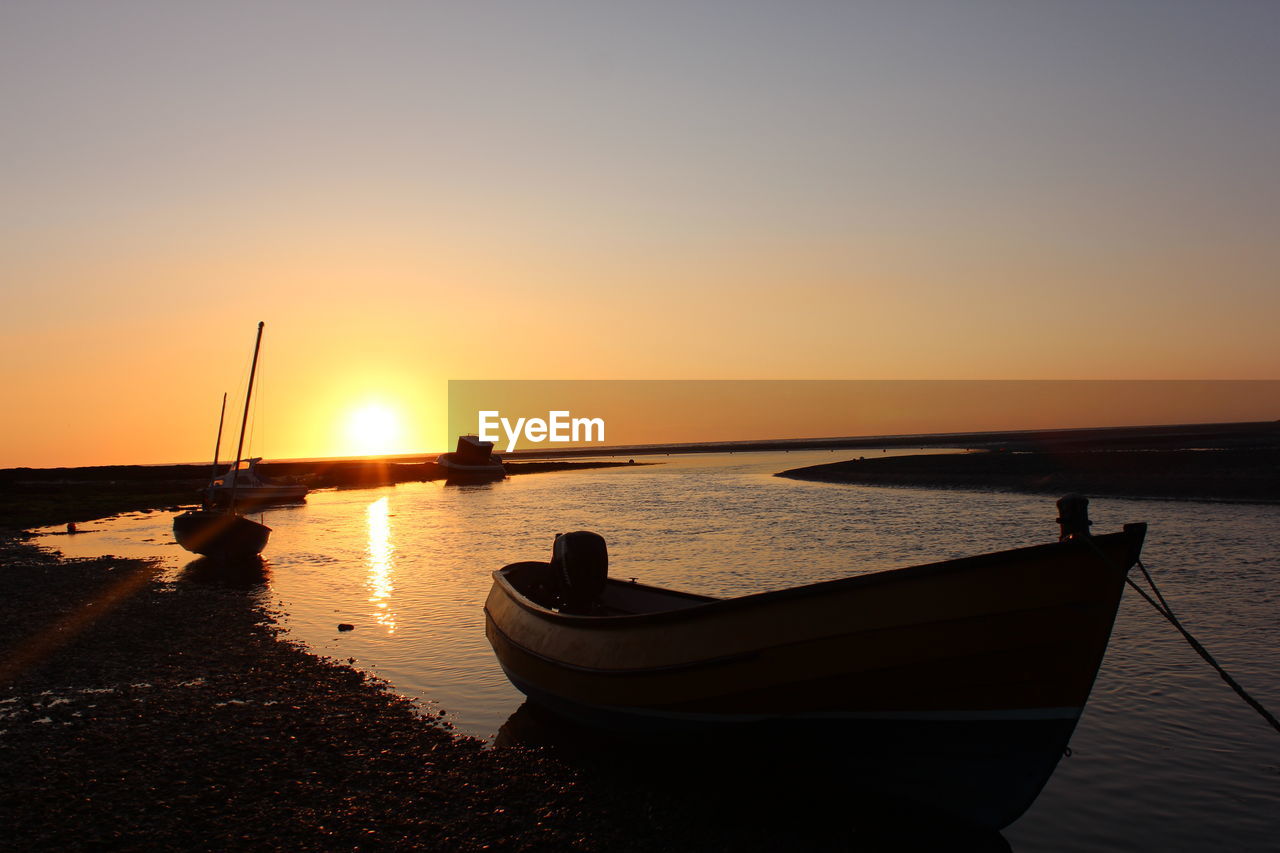 Boats moored at sea against clear sky during sunset