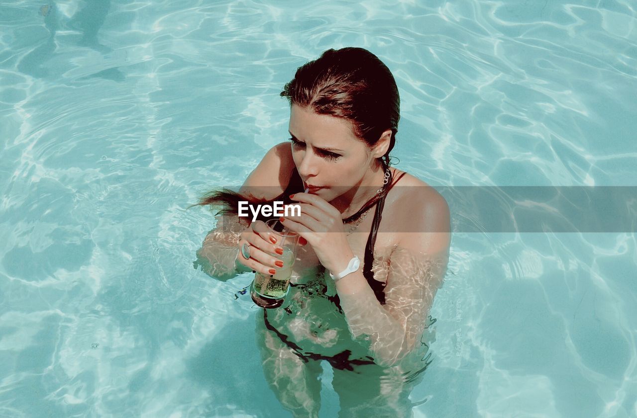 High angle view of woman sipping drink in swimming pool