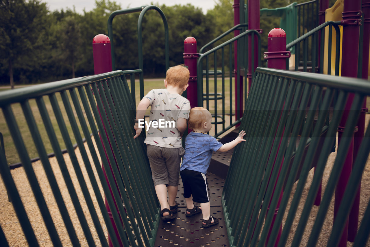 Rear view of brothers walking on jungle gym at playground