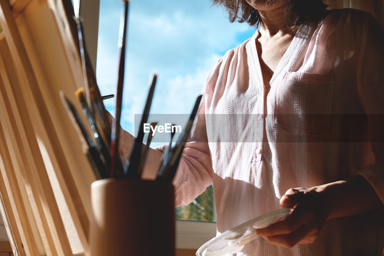 Woman painting picture on canvas at easel near the window in the studio. art painting hobby. 