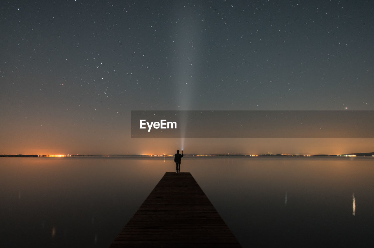 Man standing on pier over lake against sky at night