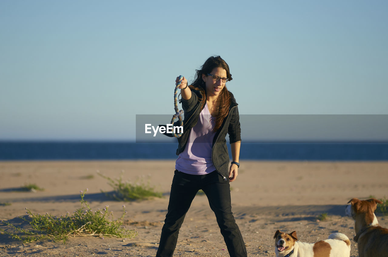 Woman playing with dogs at beach against blue sky