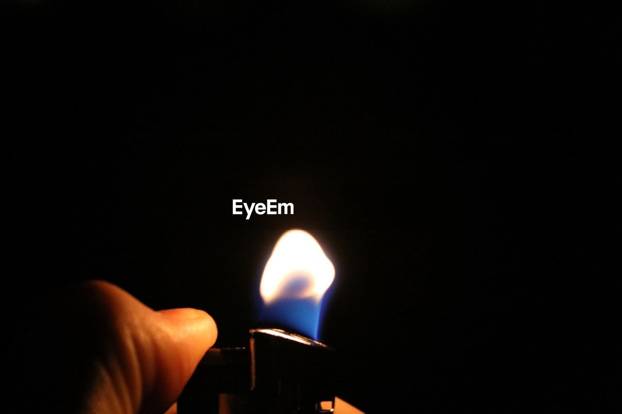 Cropped hand igniting cigarette lighter in darkroom