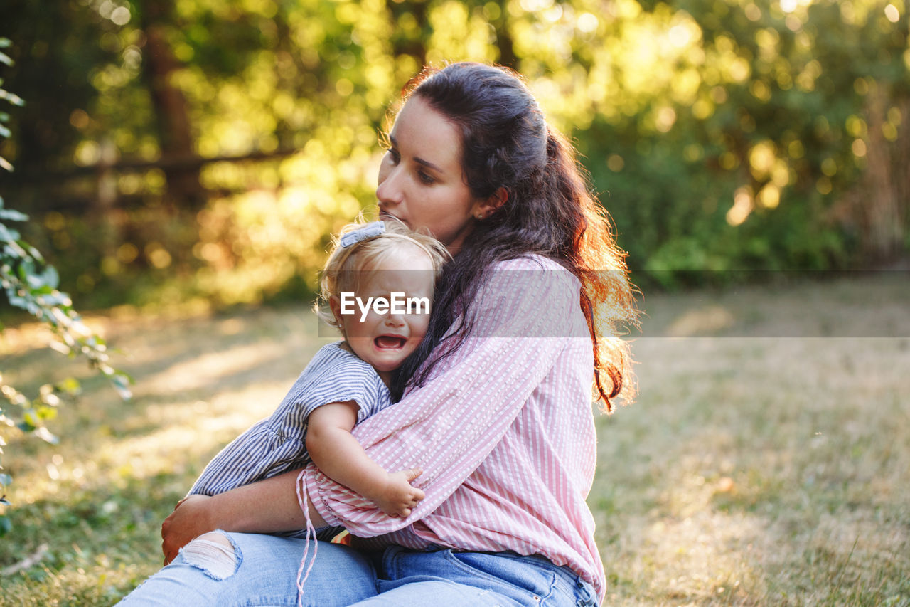 Mother hugging pacifying sad upset crying toddler girl. family young mom and crying baby in park 