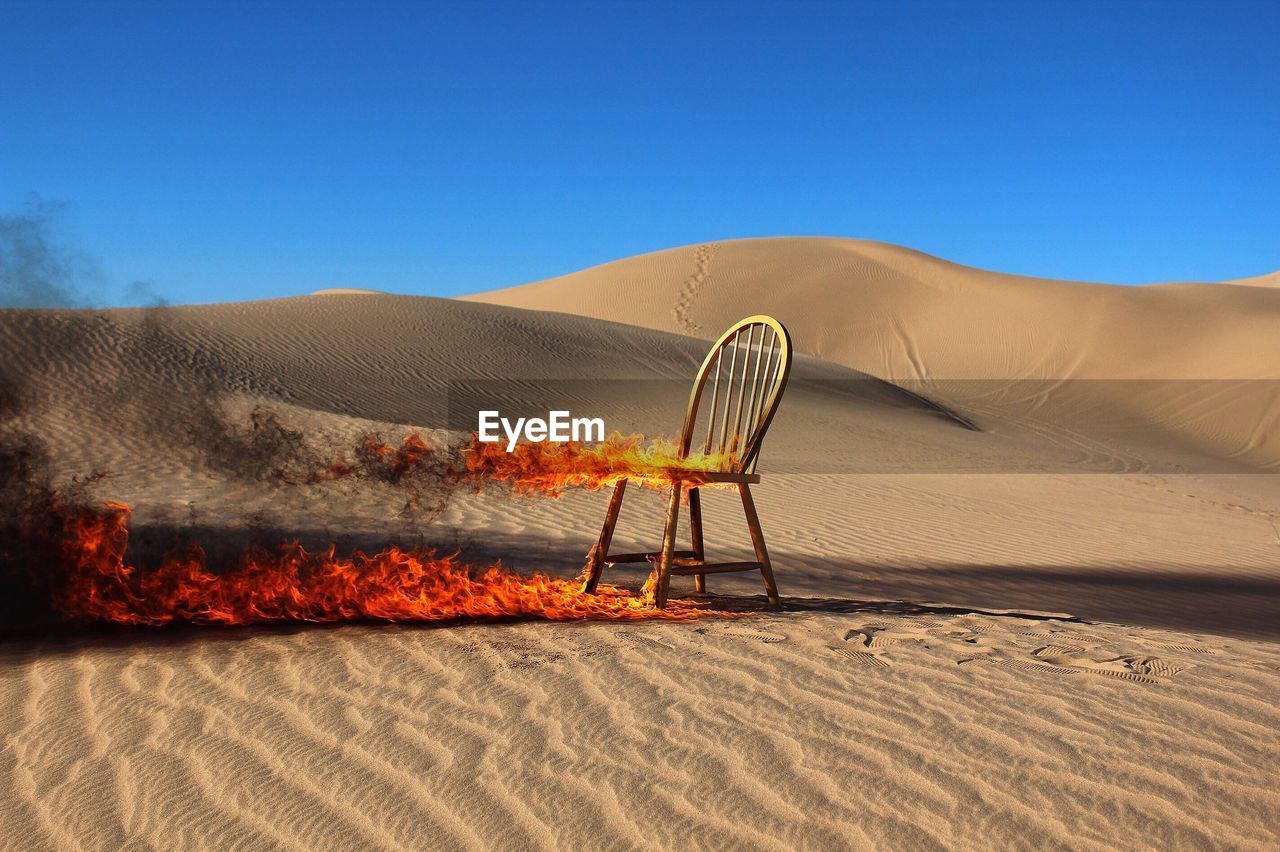 Burning chair in desert against clear blue sky