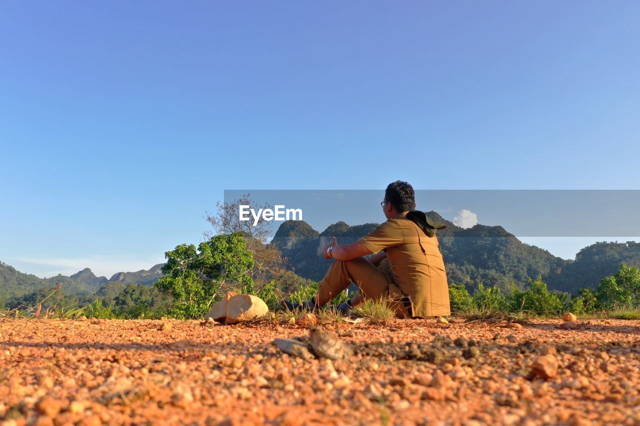 Man sitting on land against clear sky