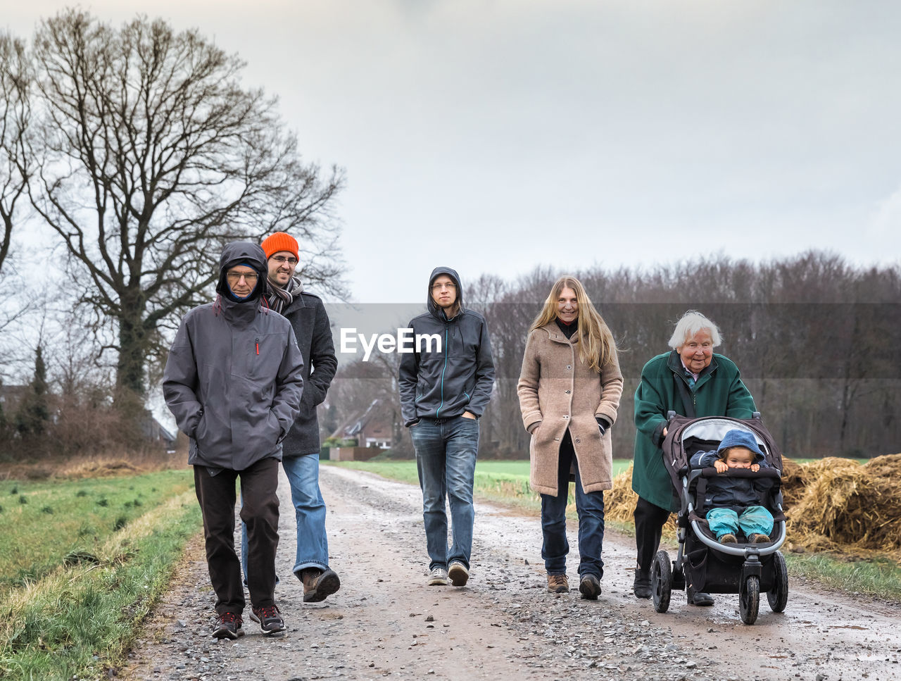 Full length portrait of multi-generation family walking on dirt road against sky during winter
