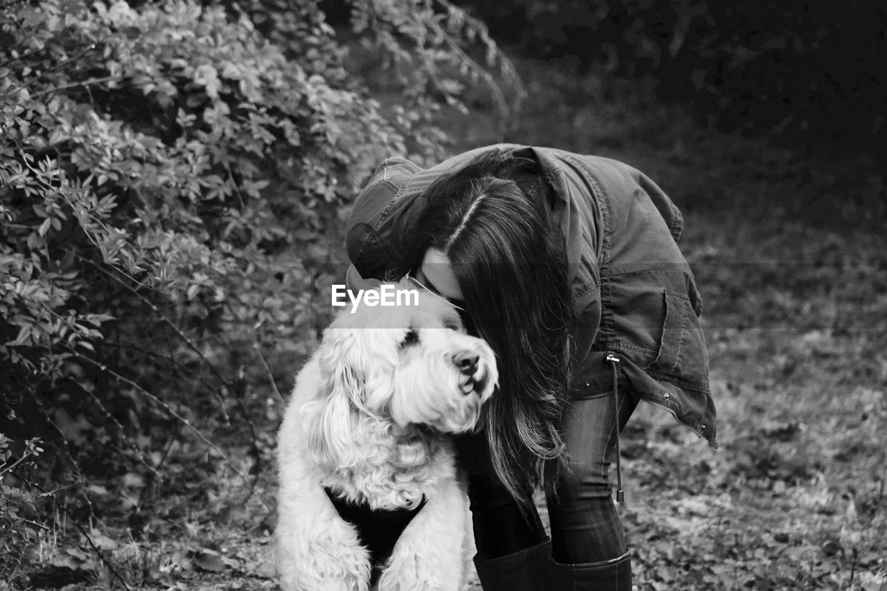 Woman kissing dog while standing on field