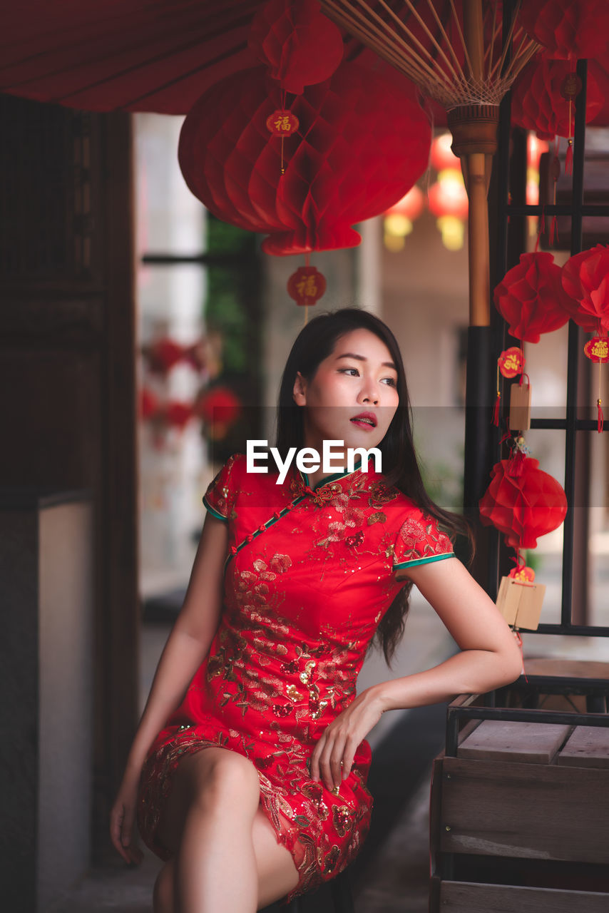 Beautiful woman in dress looking away while sitting at home