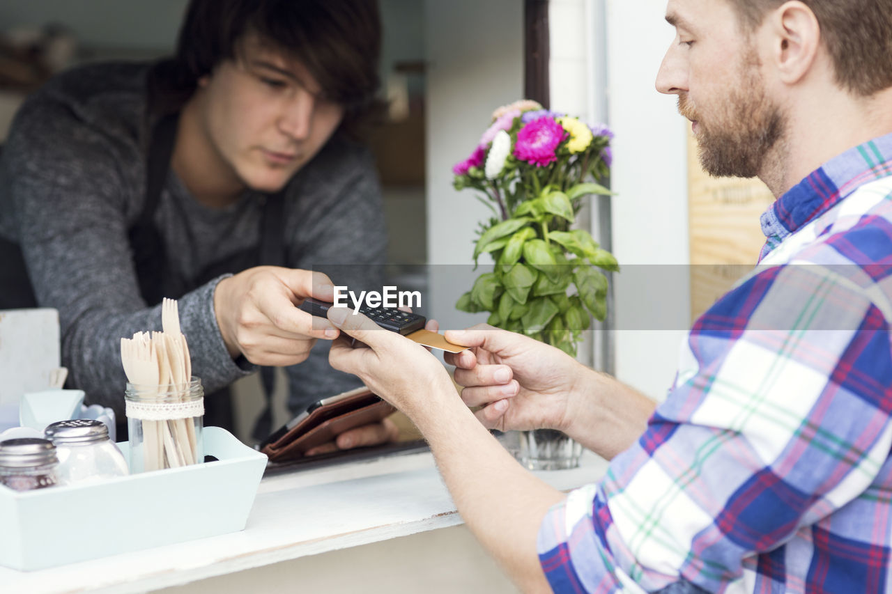 Male owner accepting payment through credit card reader from customer at food truck