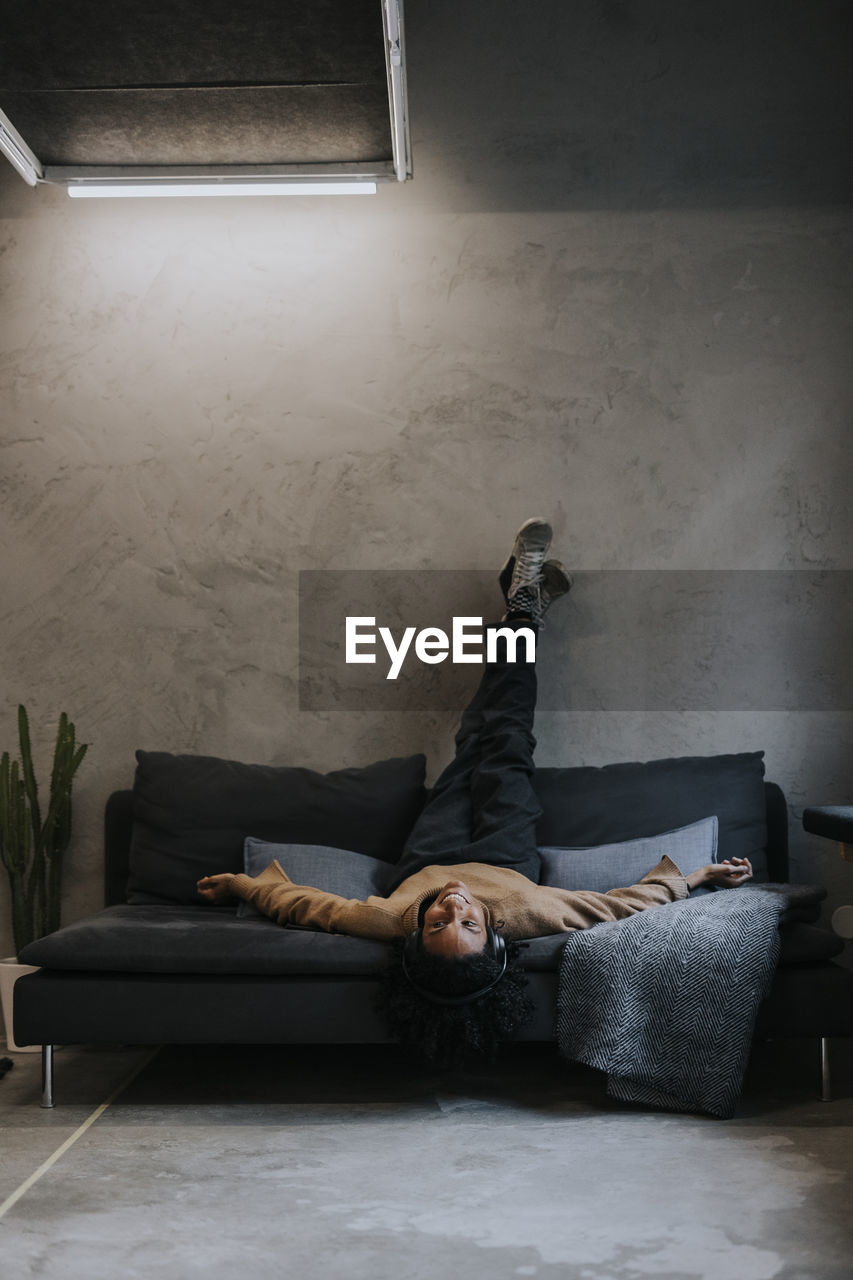 Businesswoman lying upside down on sofa against wall in creative office