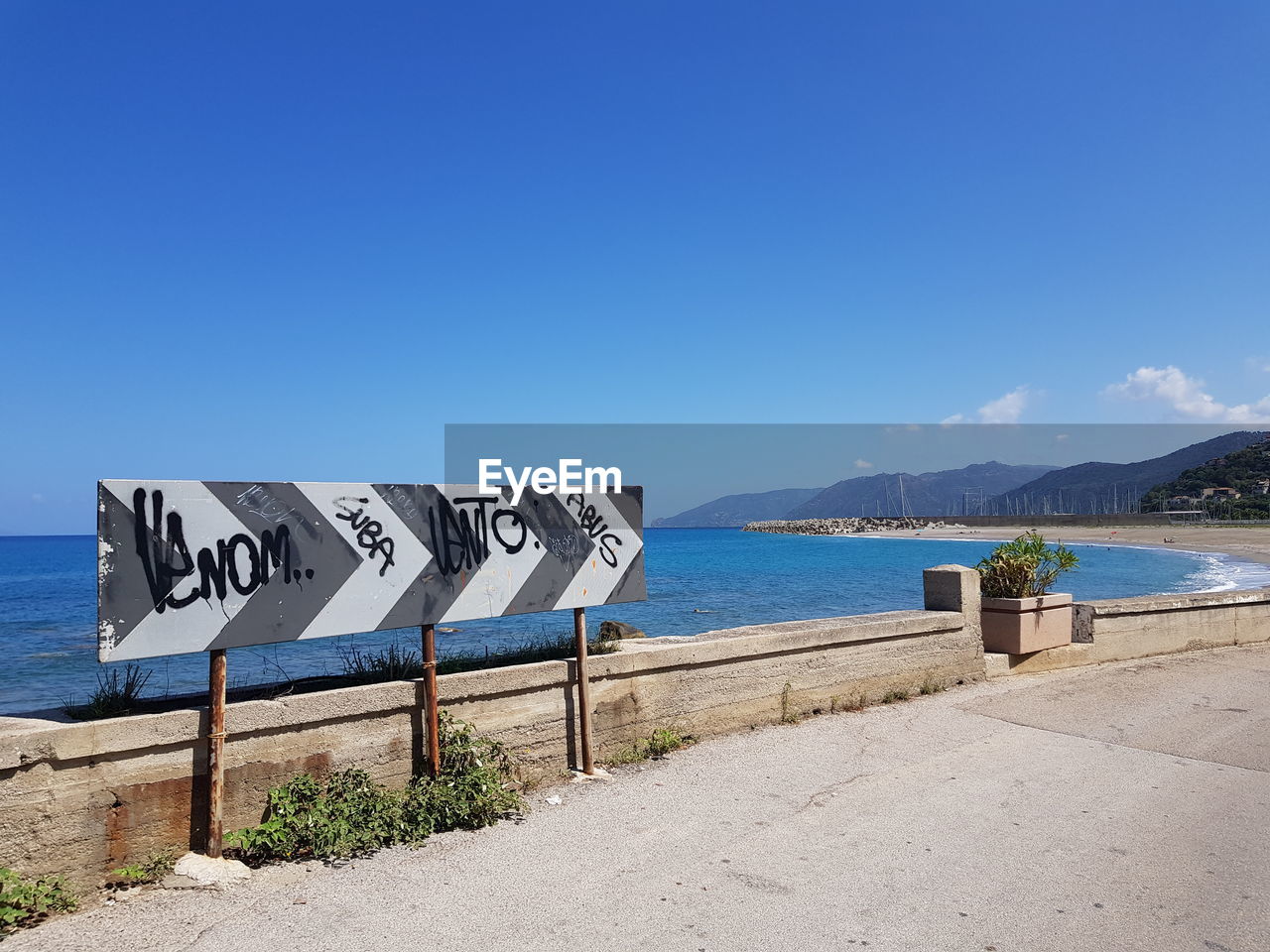 Scenic view of sign by sea against clear blue sky