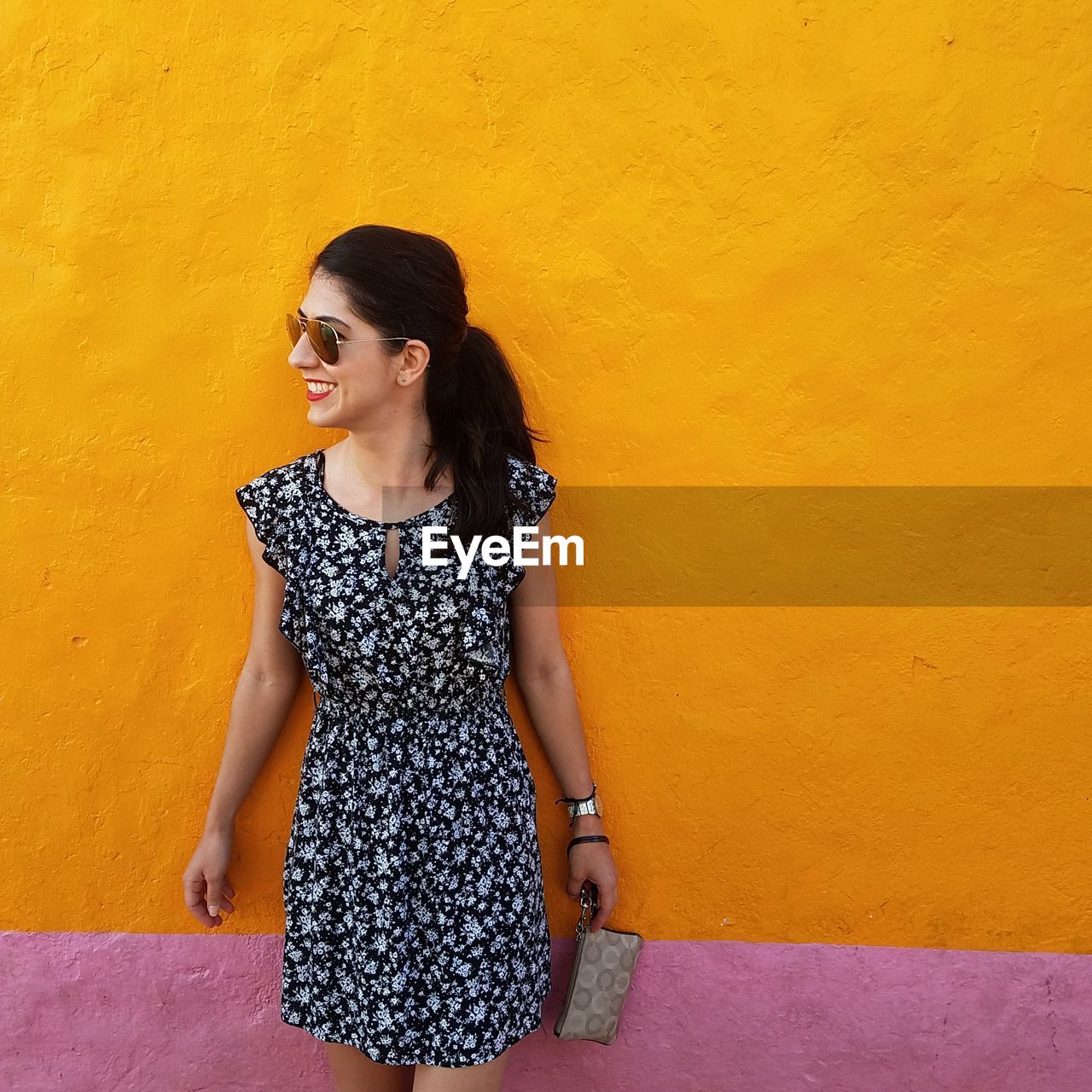 Smiling woman wearing sunglasses while standing against orange wall