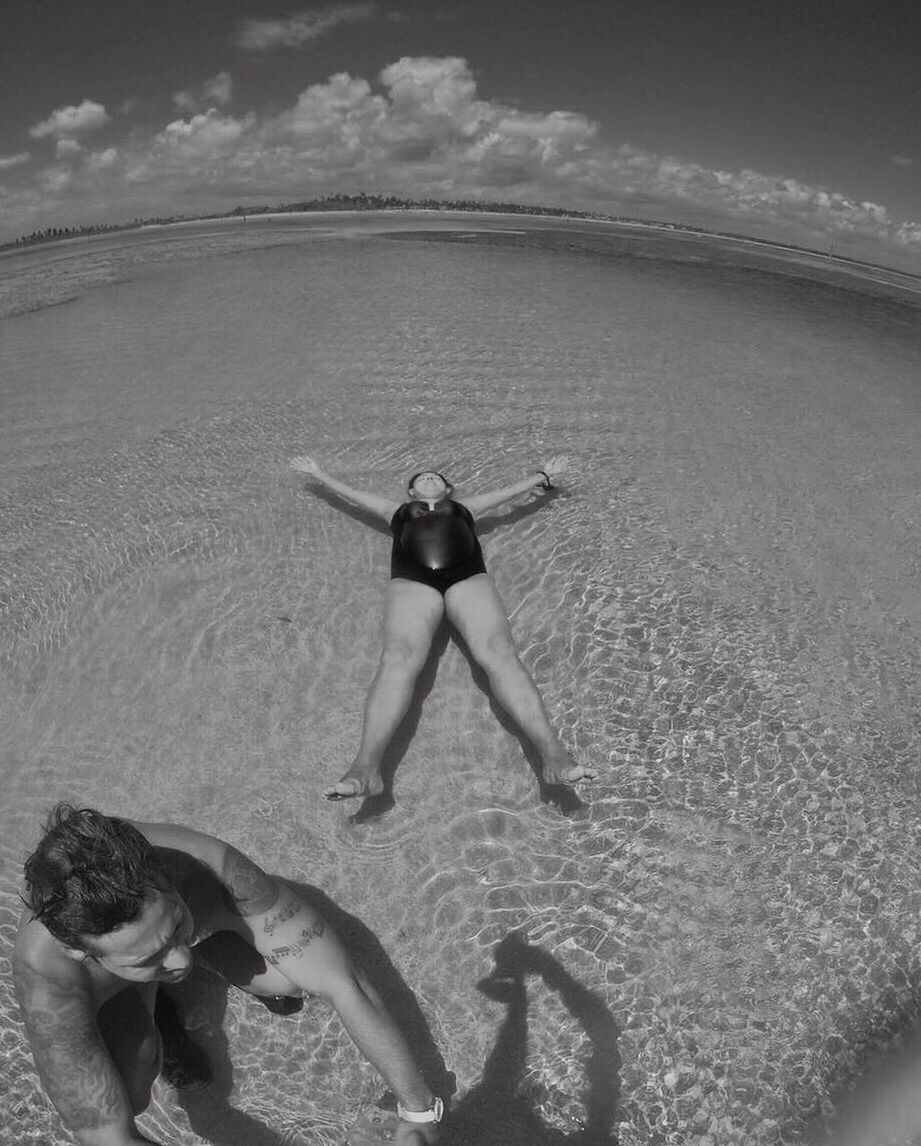 REAR VIEW OF WOMAN WITH ARMS RAISED ON BEACH