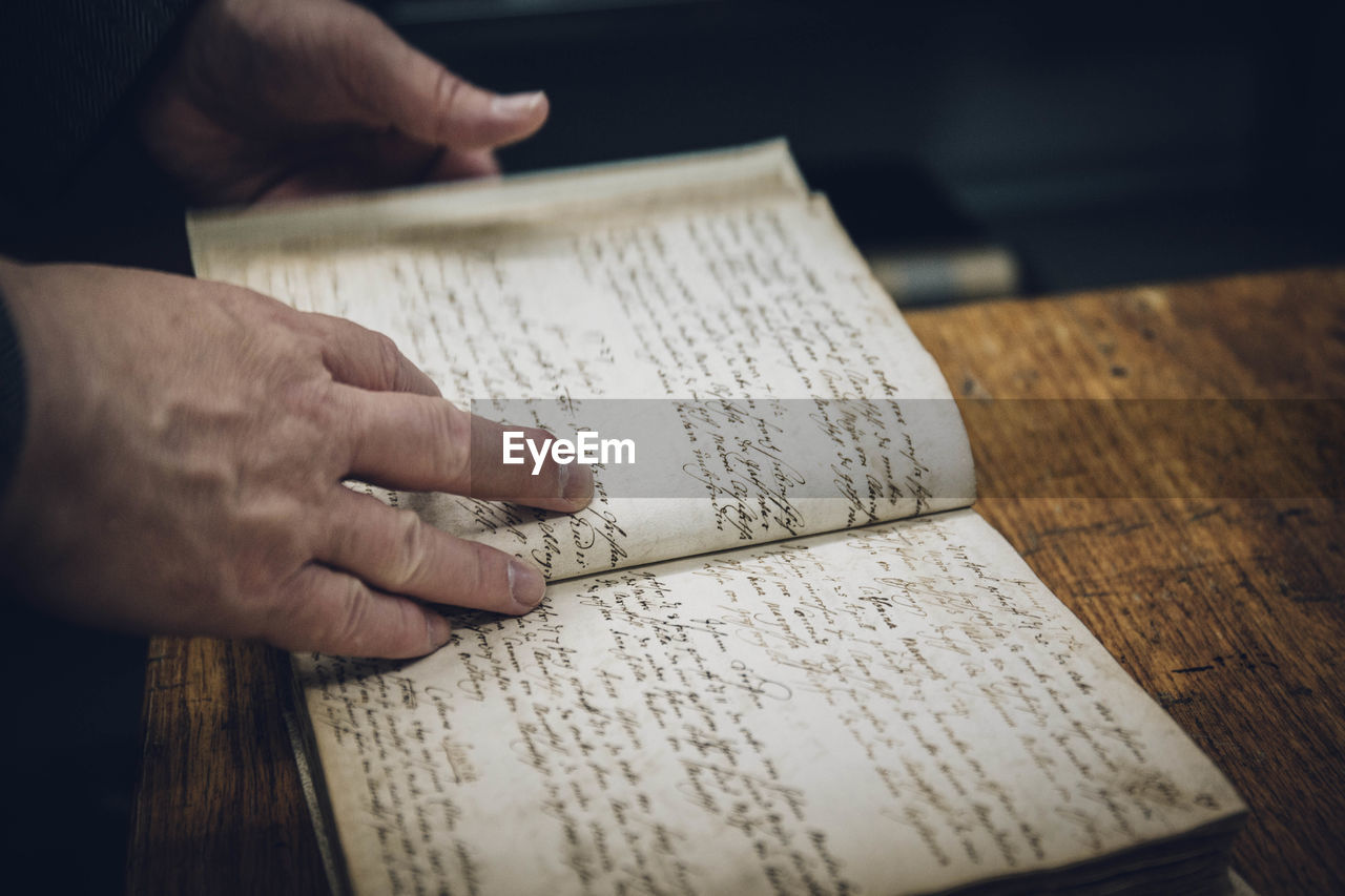 CROPPED IMAGE OF HAND HOLDING BOOK ON TABLE