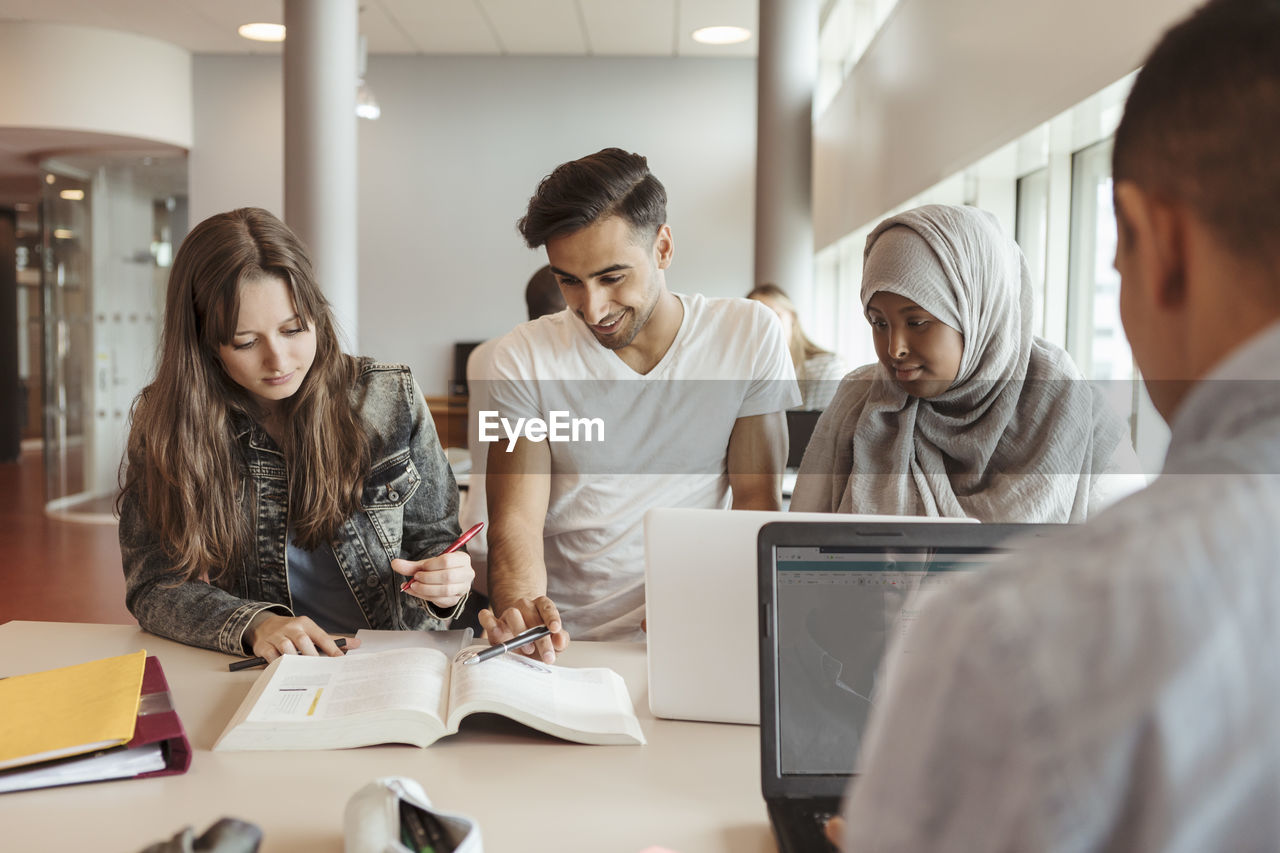 Multi-ethnic friends reading textbook at desk in university