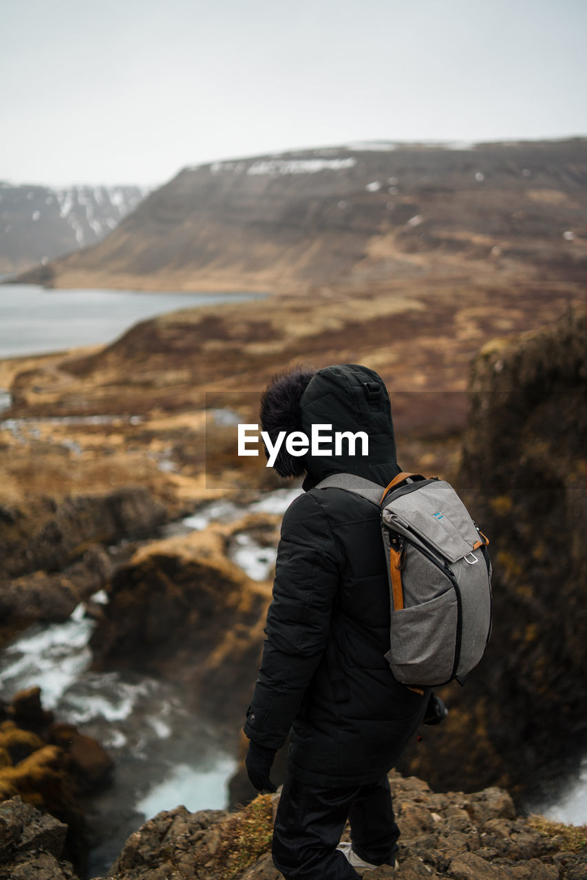 Full length of hiker standing on cliff against sky