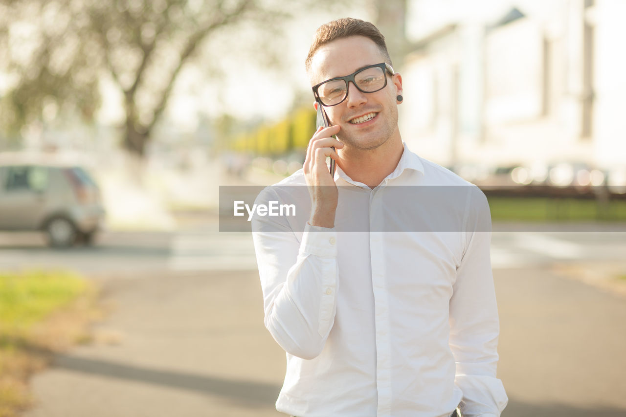 Portrait of smiling young man talking on mobile phone while standing in city