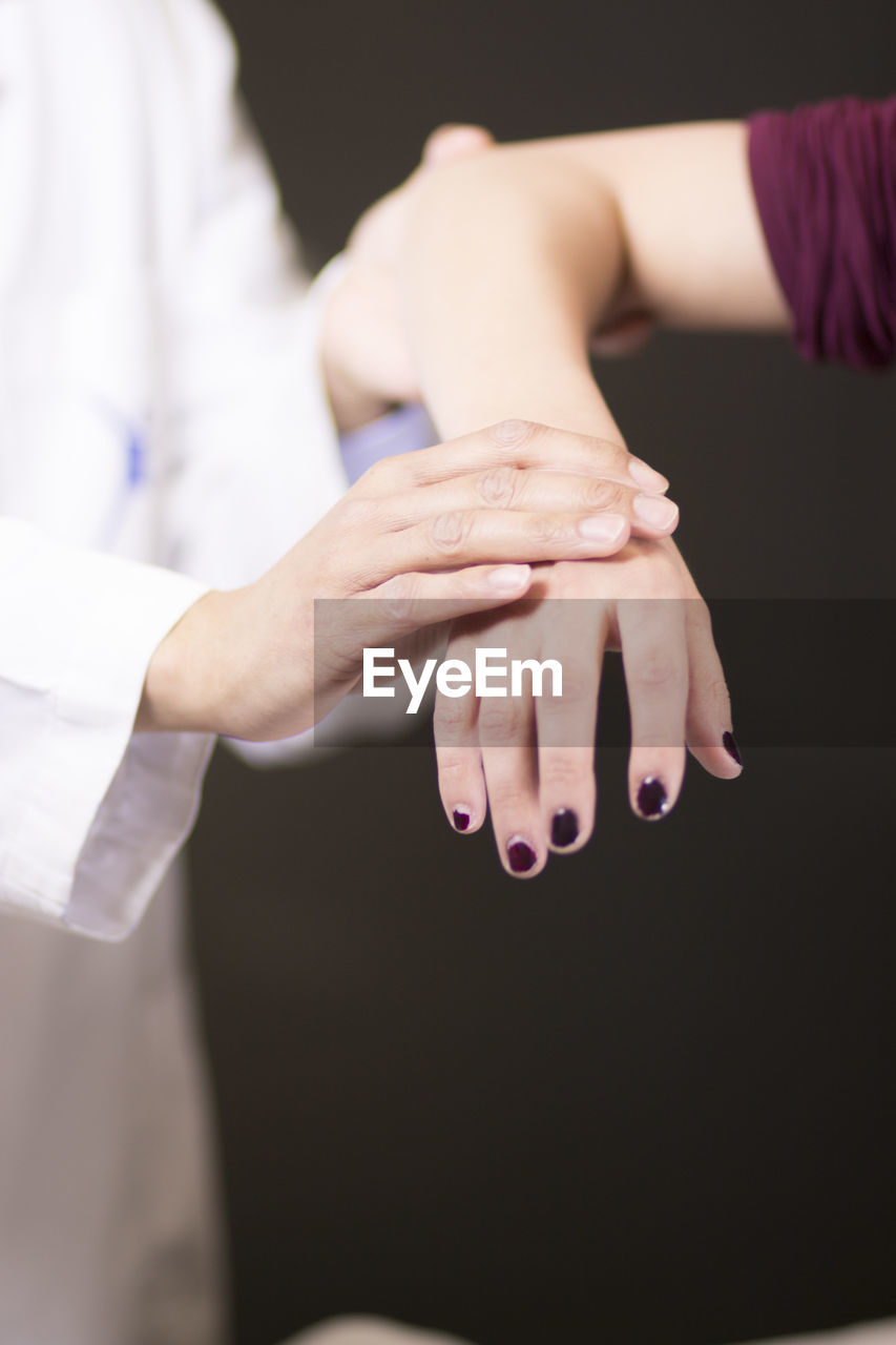 Midsection of doctor examining hand against black background