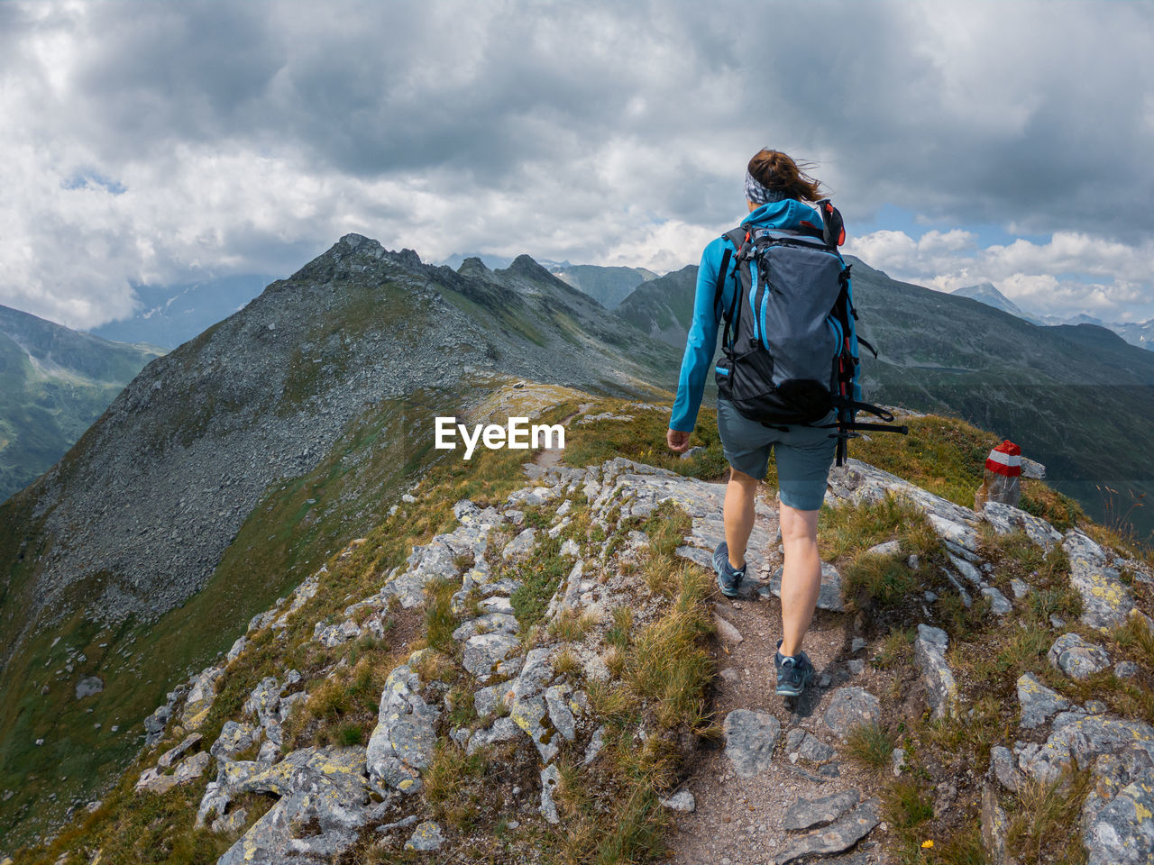 Rear view of woman hiking on rocky mountain peak against sky