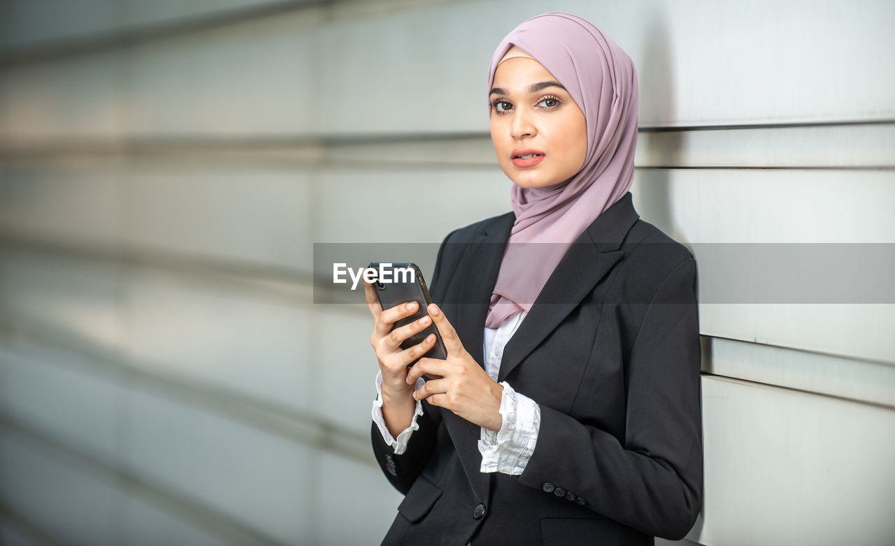 YOUNG WOMAN LOOKING AWAY WHILE STANDING AGAINST WALL