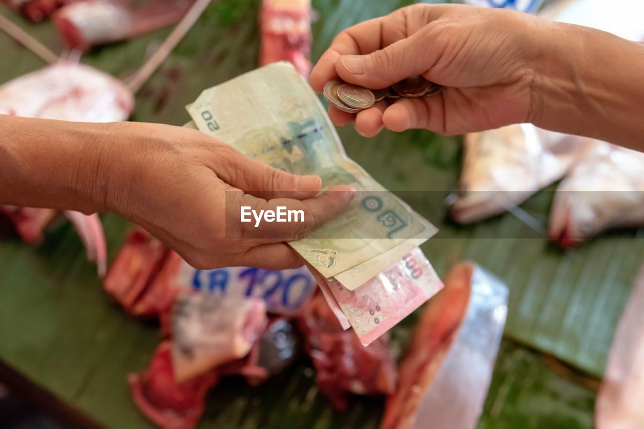 Cropped hands of person giving currency to seller at store
