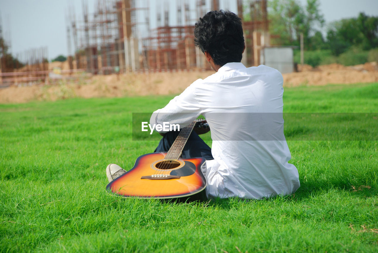 Rear view of man sitting with guitar on grass