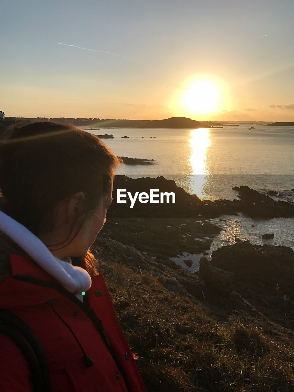 Woman looking at sea against sky during sunset from cliff