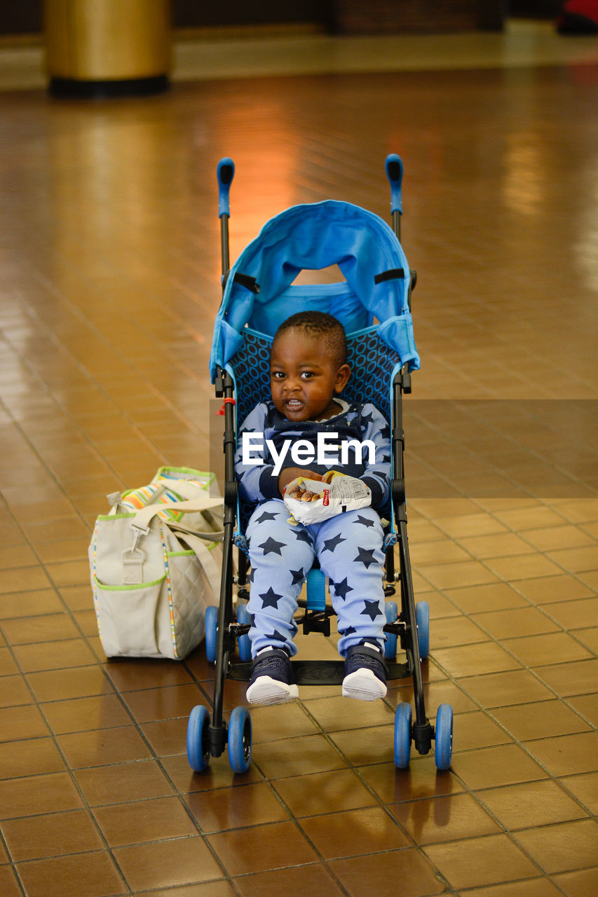 Portrait of cute toddler in baby stroller over tiled floor