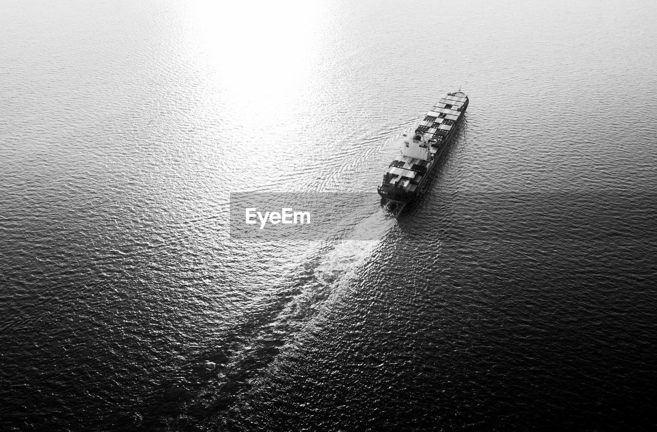 Container cargo ship in middle of the sea and over the sunlight at evening, black and white 