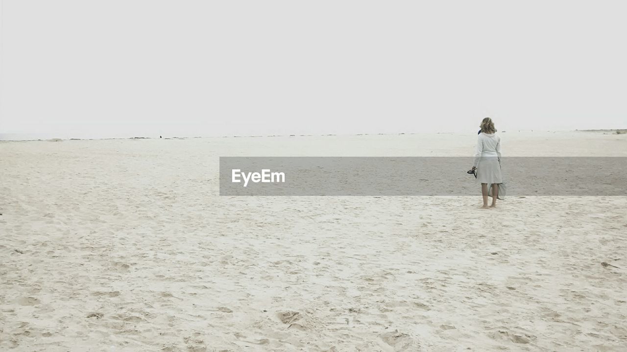 Rear view of woman standing on beach against sky