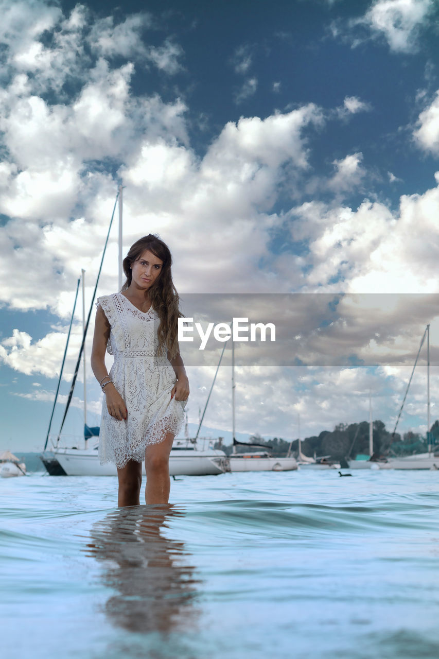 Woman holding sailboat in sea against sky