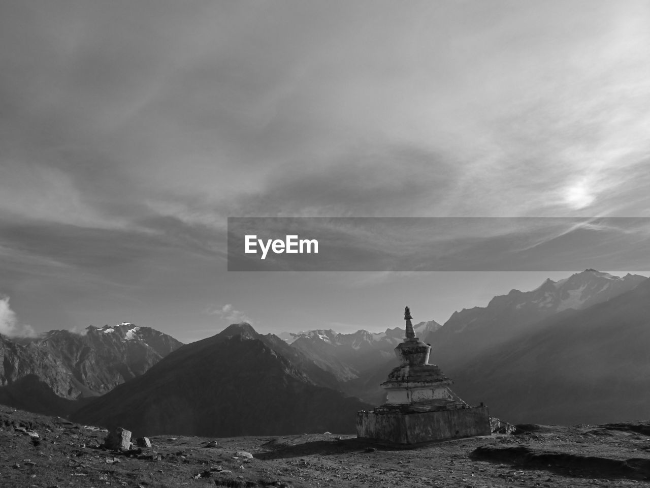 Stupa on mountain against cloudy sky during sunny day