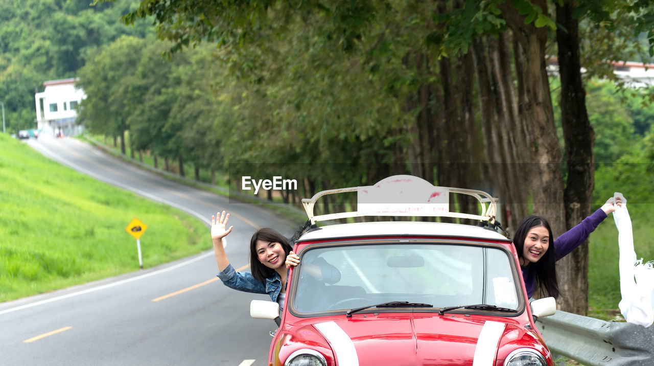 Portrait of smiling friends peeking through car window