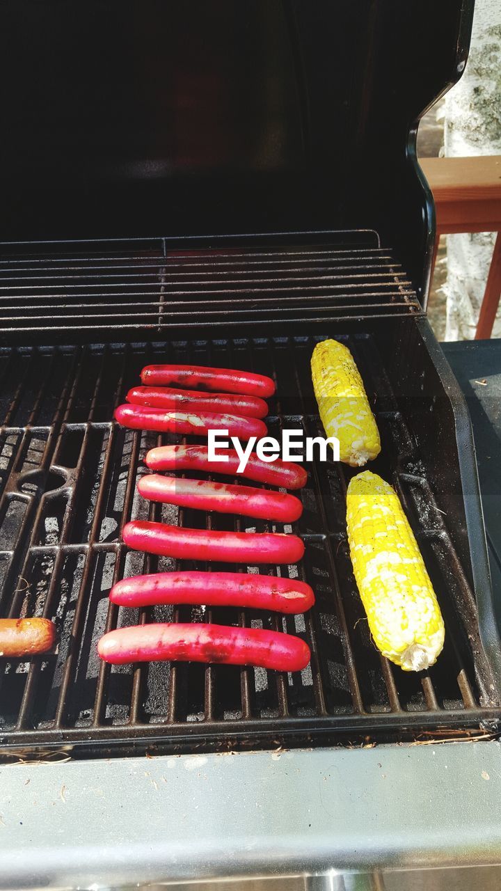 High angle view of sausages and corns on barbeque grill