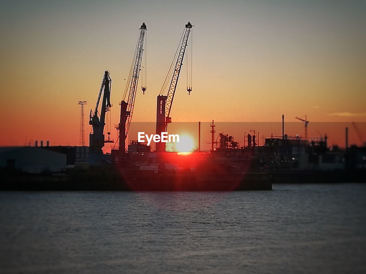 CRANES AT COMMERCIAL DOCK AGAINST SKY AT SUNSET