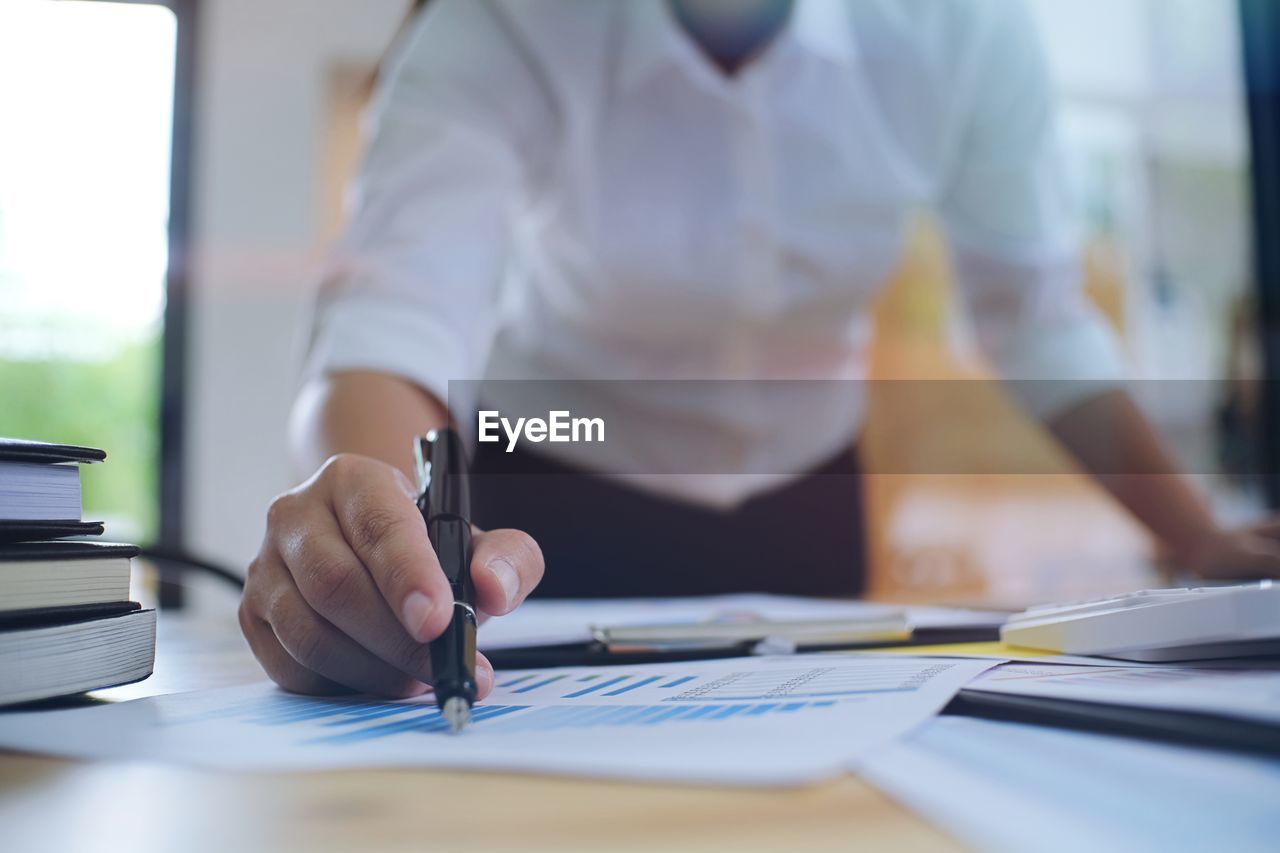 Midsection of businesswoman analyzing graphs at table in office