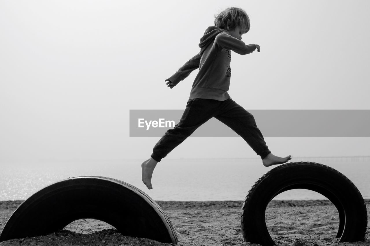 Side view of boy jumping in tire at beach against sky