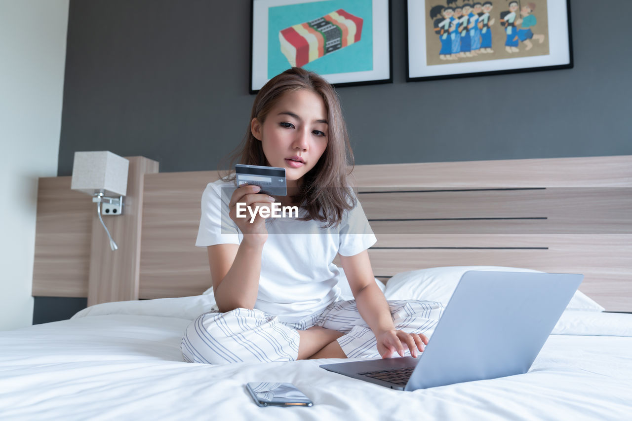 young woman using mobile phone while sitting on bed