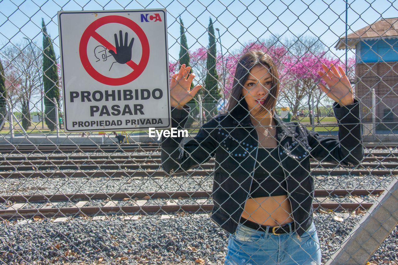 Portrait of woman standing by chainlink fence